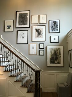 there are many framed pictures on the wall next to the stair case in this house