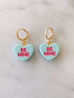 Obsessed is an understatement! Pay homage to your favorite Valentine's Day candies with these adorable be mine huggies. Available in both pierced hoops or clip on styles (for those without their ears pierced) these earrings are super fun and eye catching. Choose from a matte candy heart in a number of different colors or a two color glitter heart. The perfect size they are noticeable without being overwhelming. The charms are lightweight and easy to wear. Hoops are gold plated and nickel free. M Personalized Earrings For Valentine's Day, Trendy Huggie Heart Earrings For Valentine's Day, Cute Heart Charm Huggie Earrings, Cute Single Earring Jewelry For Valentine's Day, Cute Single Earring For Valentine's Day, Cute Huggie Earrings With Heart Charm, Single Earring For Valentine's Day, Cute Heart Charm Earrings For Anniversary, Valentine's Day Heart Huggie Earrings With Matching Set