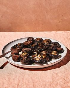 a white plate filled with cooked mushrooms on top of a brown table cloth next to a wooden spoon