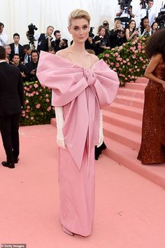 a woman in a pink gown standing on a pink carpet