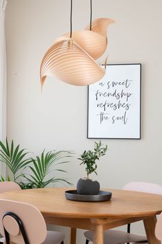 a wooden table with four chairs and a plant on top of it in front of a white wall