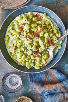 a bowl filled with green beans and bacon on top of a blue plate next to a spoon