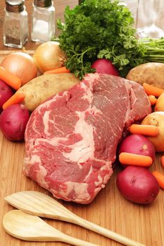 a piece of meat sitting on top of a wooden cutting board next to potatoes and carrots