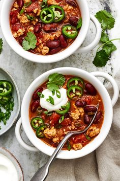 two bowls filled with chili, beans and sour cream sitting on top of a table