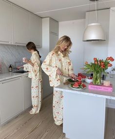 two women in pajamas are preparing food on the kitchen counter and one is cutting strawberries