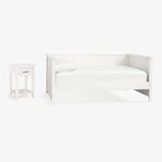 a small white bed and night stand next to each other