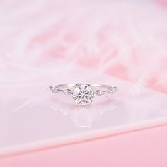 a diamond ring with three stones on it sitting on a pink surface in front of a white background