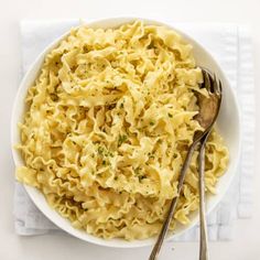 a white bowl filled with macaroni and cheese on top of a napkin next to two spoons