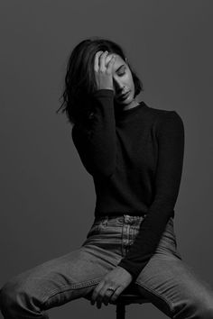 a woman sitting on top of a chair with her hands to her face, wearing jeans and a sweater