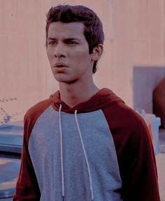 a young man wearing a hoodie standing in front of a building and looking at the camera