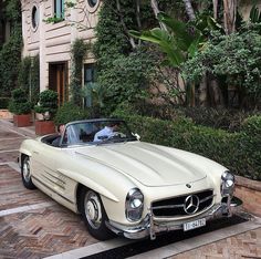 a white mercedes benz roadster parked in front of a building with trees and bushes