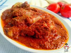 a white plate topped with meat covered in sauce next to some tomatoes and lettuce