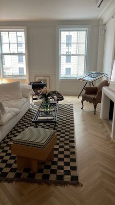 a living room filled with furniture next to two large windows on the side of a wall