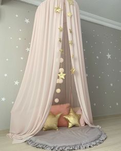 a pink canopy bed with gold stars on the ceiling and pillows in front of it