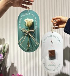 two tags with flowers attached to them are being held by someone's hand and another tag has a flower on it