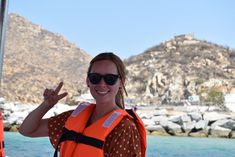 a woman in an orange life jacket on a boat giving the peace sign with her hand