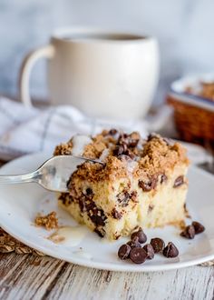 a piece of cake on a plate with chocolate chips and a cup of coffee in the background