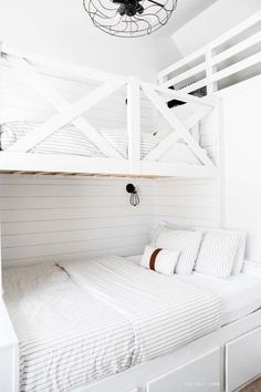 a bed with white sheets and pillows under a light fixture hanging from the ceiling above it