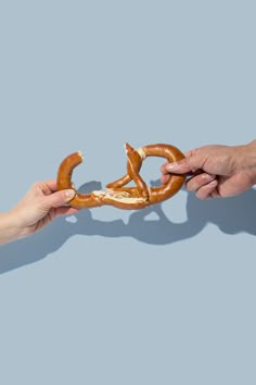 two hands reaching out to grab a pretzel from another person's hand