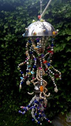 a wind chime with beads hanging from it's side in front of some bushes