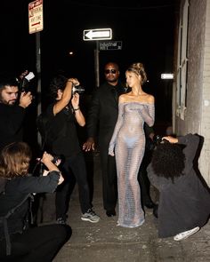 a woman in a fishnet dress is surrounded by photographers as she walks down the street