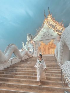 a woman walking down some stairs in front of a white building with dragon statues on it