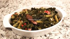 a white bowl filled with greens and meat on top of a marble countertop next to a wooden spoon