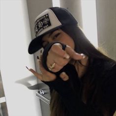 a woman with long hair wearing a hat and pointing her finger at the camera while standing in front of a sink