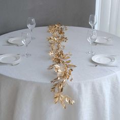 the table is set with white plates and silverware, gold leaf garland on it