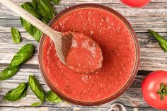 a spoon full of tomato sauce next to tomatoes and basil leaves on a wooden table