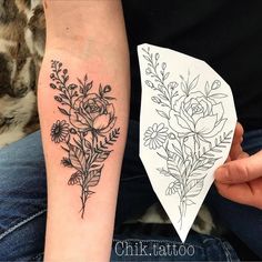 a woman's arm with flowers on it and a piece of paper in front of her