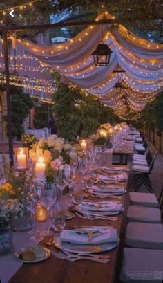 a long table set with place settings and candles for an outdoor wedding reception in the evening