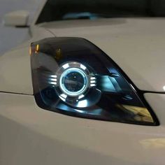 the front end of a white car with its lights on