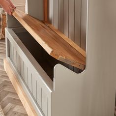 a person is holding a piece of wood near a shelf with drawers on the bottom