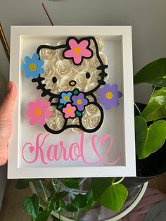 a person holding up a hello kitty cutout in a frame with flowers on it