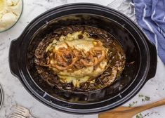 a crock pot filled with meat and cheese on top of a table next to bowls of mashed potatoes