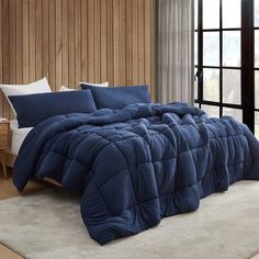 a bed with blue comforter and pillows in a room next to a wooden wall