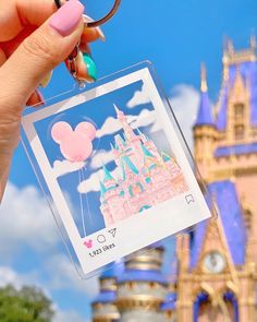 a person holding up a disney mouse keychain with a castle in the background