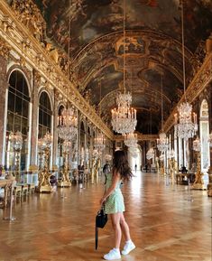 a girl in a green dress is walking through an ornate hall with chandeliers