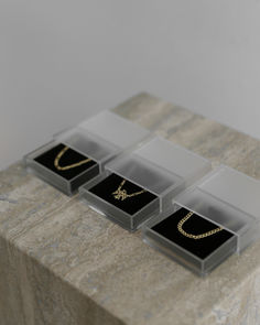 three jewelry boxes sitting on top of a marble table with gold chains in each box