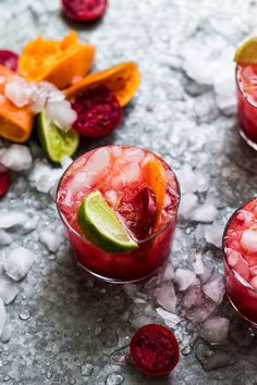 three glasses filled with drinks and garnished with fruit on the rim, sitting on crushed ice