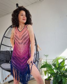 a woman in a crocheted dress is holding a blue and purple object while standing next to a hammock