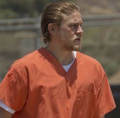 a man in an orange prison uniform looking off to the side with his hair pulled back