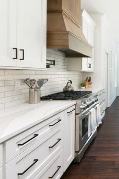 a kitchen with white cabinets and wood flooring on the walls, along with stainless steel range hoods