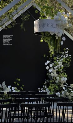 an outdoor ceremony area with black chairs and white flowers hanging from the ceiling, surrounded by greenery