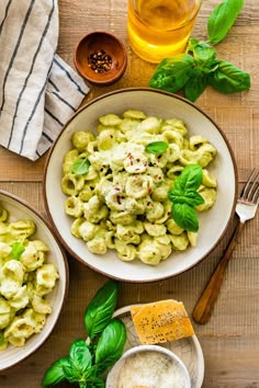 two bowls of pasta with basil and parmesan cheese on the side, next to a glass of beer