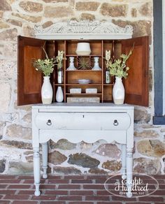 a white table with vases on top of it in front of a stone wall