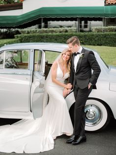 a bride and groom pose in front of an old car with the door open for their wedding photo