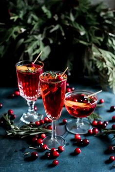 two glasses filled with red wine and garnished with cranberries on a table