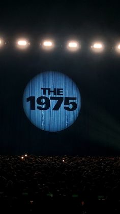 A curtain at a concert has the band logo "The 1975" projected onto it. The 1975 Background, The 1975 Aesthetic Poster, 1975 Concert Aesthetic, The 1975 Wallpaper Iphone, The 1975 Wallpaper Aesthetic, Avicii Tattoo